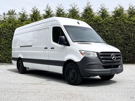A 2023 Mercedes-Benz Sprinter van with a white exterior and black accents, showcasing its large cargo area and front grille design.