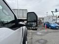 A 2018 Ford F-550 truck with a prominent side mirror is parked in a lot next to a blue car and behind a large shipping container