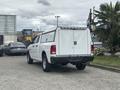 A white 2016 RAM 1500 pickup truck with a cap on the bed parked on a paved surface