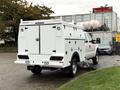 A 2015 Ford F-350 SD with a white service body and compartments on the sides parked in a commercial area
