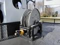 A metal hose reel on a sturdy base with coiled black hose and a yellow connector on the side
