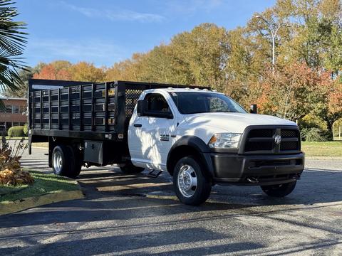 A white 2015 RAM 4500 truck with a black flatbed and metal grid sides is parked, showcasing its robust design and heavy-duty capabilities