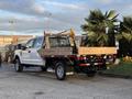 A 2018 Ford F-350 SD with a flatbed design featuring wooden planks and lights on the rear side is parked and facing to the right