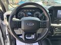 Steering wheel of a 2021 Ford F-150 with controls and Ford logo visible in the center alongside a digital dashboard displaying speed and other metrics