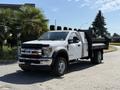 A white 2019 Ford F-550 truck with a flatbed and black dump body parked on a street