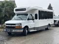 A 2018 Chevrolet Express van with a white exterior and large windows designed for passenger transport parked on a wet surface