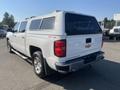 A white 2015 Chevrolet Silverado 1500 pickup truck with a cap on the bed has four-wheel drive lettering and a chrome Chevrolet logo on the rear
