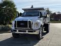 A 2017 Ford F-650 Super Duty dump truck with a silver body and black grille parked at an angle showing its front and side features