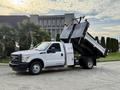 A white 2015 Ford F-350 truck with a dump bed in the upright position