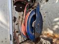 A blue hose reel with red hoses coiled inside mounted on a rusty surface