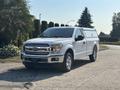 A white 2019 Ford F-150 pickup truck parked with a cap over the bed visible chrome grille and headlights
