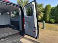 A 2016 Ford Transit 150 with its rear door open revealing a spacious cargo area with gray upholstered seats and a black rubber floor mat
