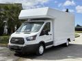 A 2016 Ford Transit van with a white box cargo body and a sloped roof, parked with its front facing the viewer