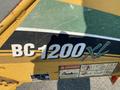 A 2010 Vermeer Corporation BC1200XL chipper with a green and yellow body and a clearly visible model number and warning labels