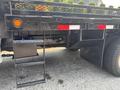 A 2009 Ford F-450 Super Duty with a flatbed and access steps on the side showing a sturdy black finish and reflective safety markings