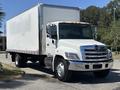 A 2020 Hino 338 box truck with a white exterior and a shiny chrome grille parked on the street