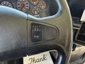 Close-up of the steering wheel of a 2013 International CE300 showing controls for cruise control on the left side with a textured black finish and a white thank you note underneath