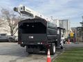 A 2012 International DuraStar 4300 bucket truck with a hydraulic lift arm extended attached to the rear and a large storage compartment at the back