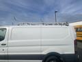 A white 2017 Ford Transit van with a silver ladder rack mounted on the roof