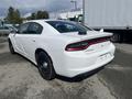 A white 2017 Dodge Charger with a black rear spoiler and black wheels parked in a lot viewed from the rear left angle