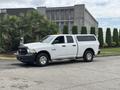 A white 2013 RAM 1500 pickup truck with a fitted cap on the bed and a yellow light on top parked on a paved surface