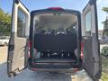 A 2025 Ford Transit T-350 with open rear doors revealing a spacious interior featuring multiple rows of seats and a flat cargo area