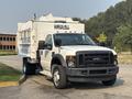 A 2009 Ford F-550 truck with a white exterior features a flatbed and a rear cargo area with a boxy design for hauling materials