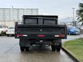 A black 2017 Ford F-450 Super Duty truck viewed from the rear with a flatbed, taillights visible, and a large dumpster in the bed