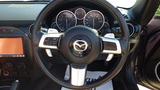 The interior dashboard of a 2007 Mazda Miata featuring a round steering wheel with a central Mazda logo and digital gauges