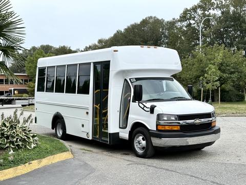 A white 2015 Chevrolet Express shuttle bus with large windows and an open door for passenger access