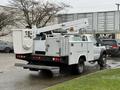 A 2006 Ford F-450 truck equipped with a large white utility bucket lift and storage compartments on the sides