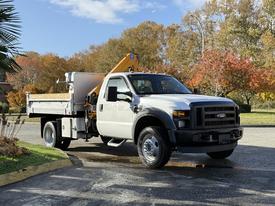 A white 2008 Ford F-550 with a flatbed and mounted crane is parked on a paved surface in a well-maintained area