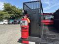 A red fire extinguisher mounted on the side of a black truck bed with a textured surface and a metal grid enclosure
