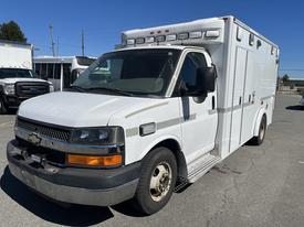 A 2013 Chevrolet Express ambulance in white with a prominent front grille and multiple emergency lights on the roof