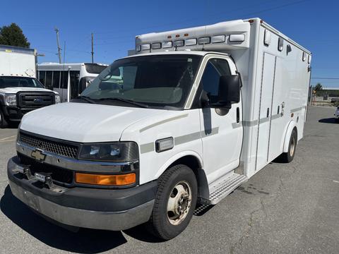A 2013 Chevrolet Express ambulance in white with a prominent front grille and multiple emergency lights on the roof