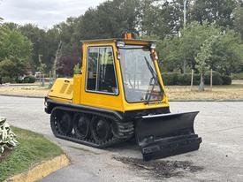 A yellow 2004 Bombardier SW48 snowplow with tracks and a black blade is parked on a paved surface designed for snow removal and maintenance tasks
