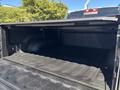 An empty truck bed of a 2015 RAM 1500 with a black lining and a cover partially open