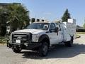 A 2015 Ford F-550 pickup truck with a white exterior and utility body featuring various equipment compartments and a front grill guard