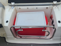 A white cooler with a red bottom is secured in a boat storage compartment with a stainless steel rail around it