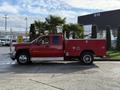 A red 2013 Chevrolet Silverado 3500HD with a utility bed and chrome wheels parked with palm trees in the background