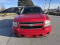 A red 2011 Chevrolet Avalanche with a prominent front grille and headlights parked on a road