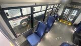 Interior view of a 2021 Ford Transit bus featuring blue seats arranged along the side with a clear view of the large windows