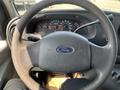 A steering wheel of a 2005 Ford Econoline with the Ford logo in the center and various dashboard gauges visible in the background