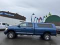 A blue 2006 Dodge Ram 2500 pickup truck with a canopy attached to the bed parked on a wet surface