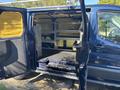 A 2016 Ford Transit 150 van with an open side door revealing a spacious interior featuring shelving and a flat surface inside