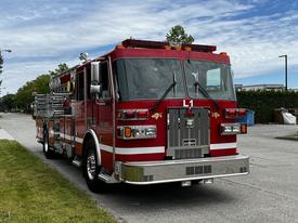 A red 2002 Sutphen Monarch fire truck equipped with ladders and firefighting tools parked on the street