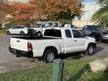 A white 2013 Toyota Tacoma pickup truck with a compact cab and bed is parked, showcasing its side and rear profile