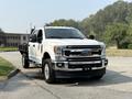 2020 Ford F-350 Super Duty pickup truck with a white exterior and chrome details parked on a street with a flatbed in the back