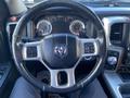 Steering wheel of a 2017 RAM 1500 featuring controls and gauges at the dashboard with a leather-wrapped design and the RAM logo in the center