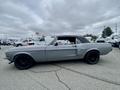 A 1968 Ford Mustang two-door convertible in gray with a black soft top and black wheels, viewed from the side